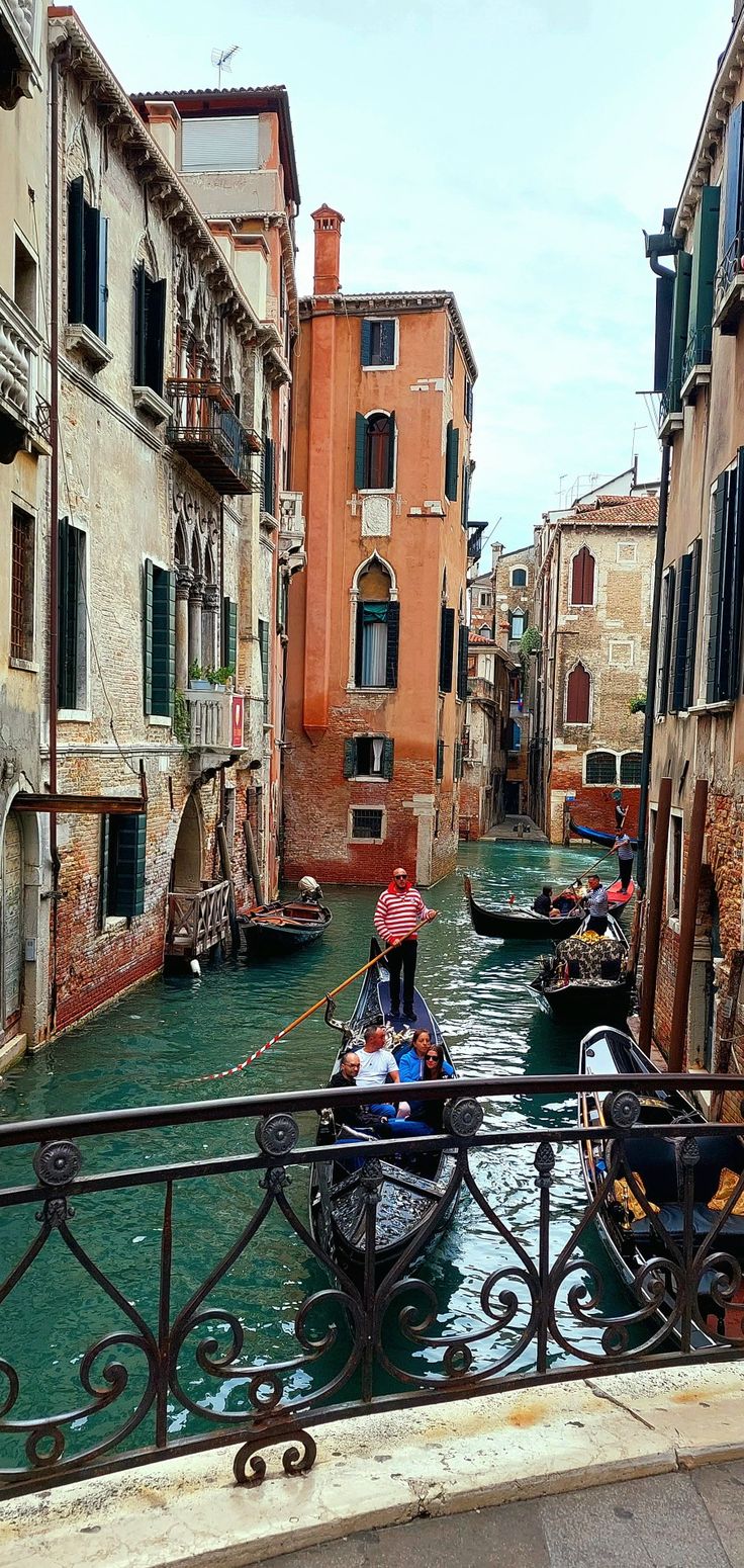 two gondolas on a narrow canal with buildings and people in the water behind them