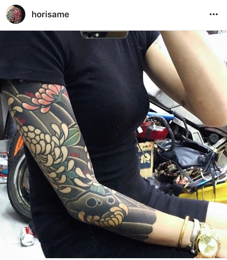 a woman with tattoos on her arm sitting next to a motorcycle