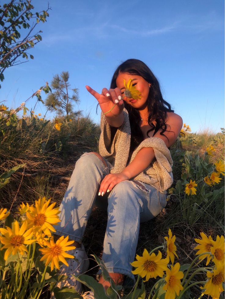 a woman sitting on the ground with her hand up to her face and yellow flowers in front of her