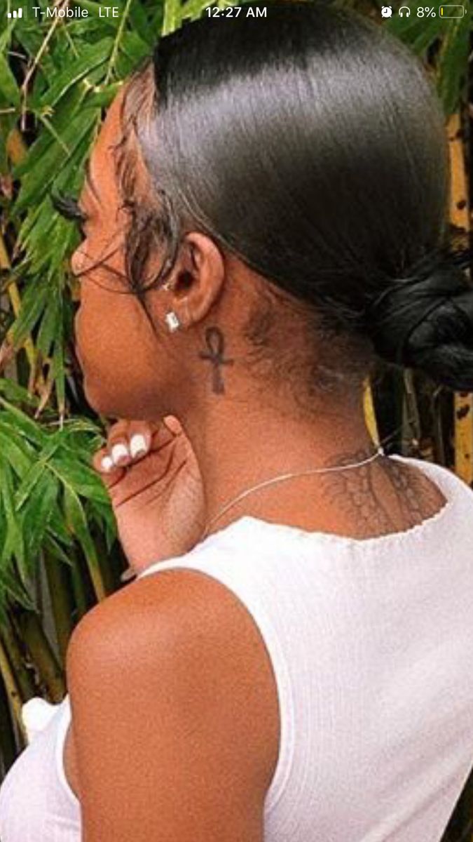 a woman with black hair wearing a white tank top and ear piercings in front of bamboo trees