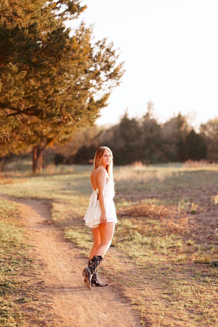 Beautiful long haired high school senior girl poses in white dress and cowboy boots turning and looking towards the camera with sunset in background on dirt trail Senior Pictures Summer, Senior Photo, Picture Collection, Senior Portrait, Senior Photographers, High School Seniors, Senior Photos, Photo Session, Senior Portraits