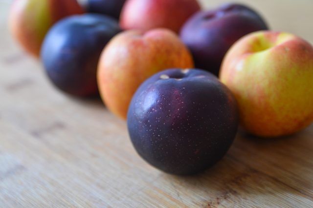 some plums and apples on a wooden table