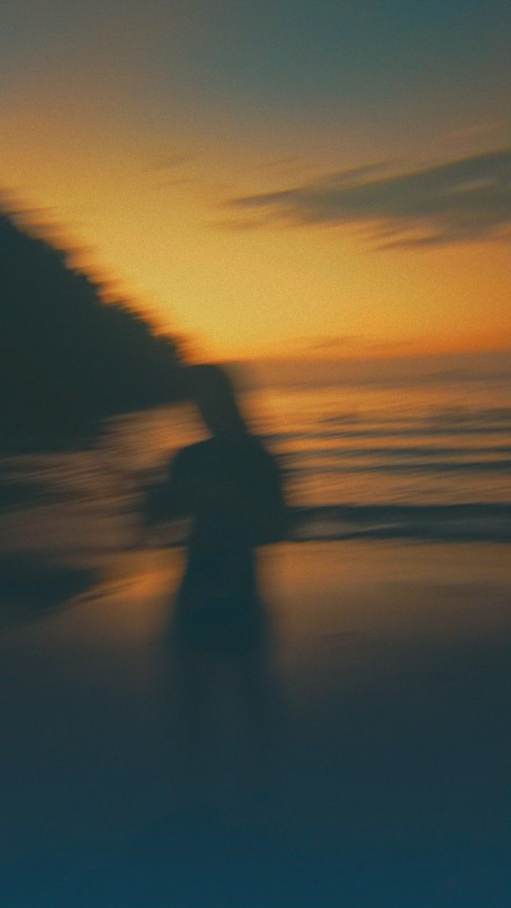 a blurry photo of a person walking on the beach at sunset or sunrise time