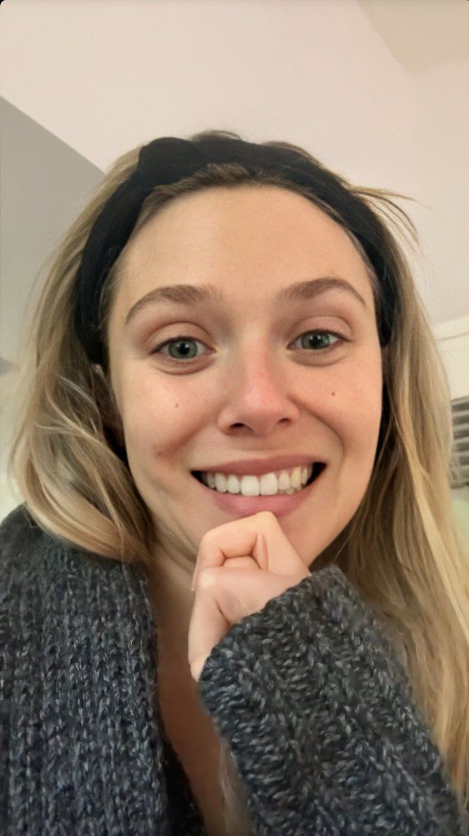 a woman with blonde hair wearing a gray sweater and black headband smiles at the camera