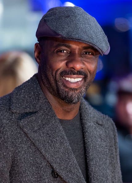 a man wearing a gray hat and jacket smiling at the camera with people in the background