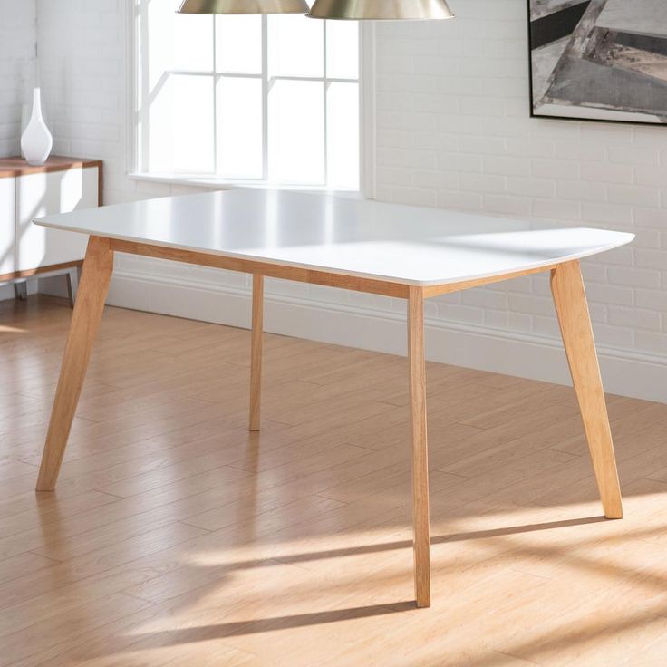 a white table sitting on top of a hard wood floor next to a painting hanging on the wall