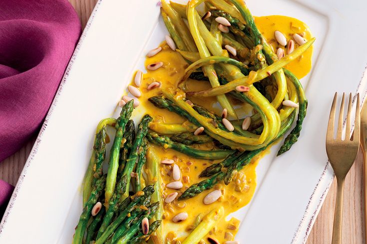 a white plate topped with asparagus covered in yellow sauce and almonds next to a fork