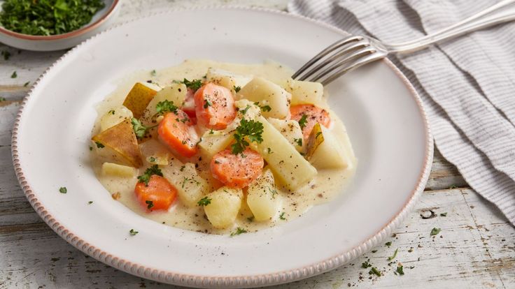 a white plate topped with potatoes and carrots next to a bowl of parsley