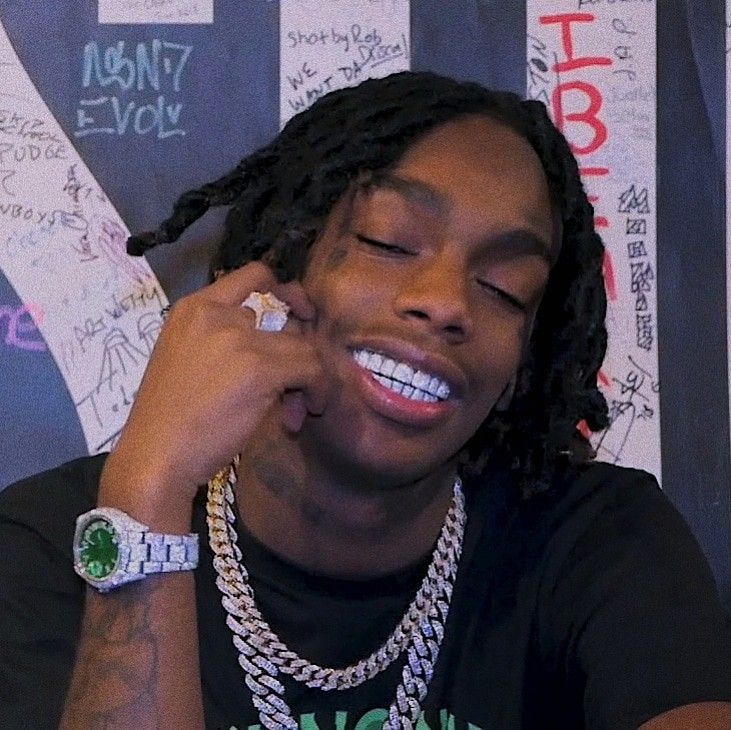 a young man with dreadlocks smiles while holding his hand to his ear