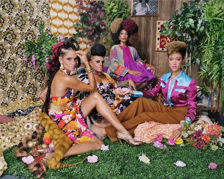 four women sitting on the ground in front of plants and flowers, all wearing colorful clothing