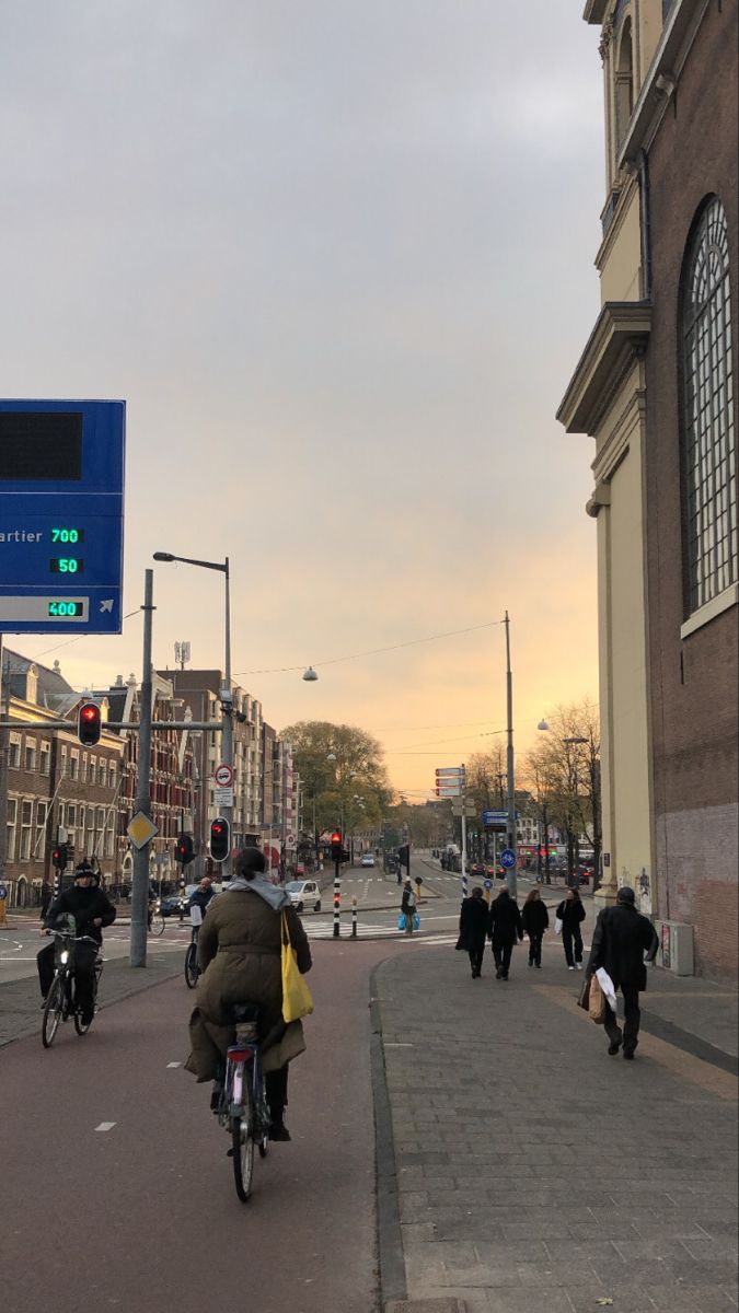 people are walking and riding bikes down the street in front of a building with a clock on it