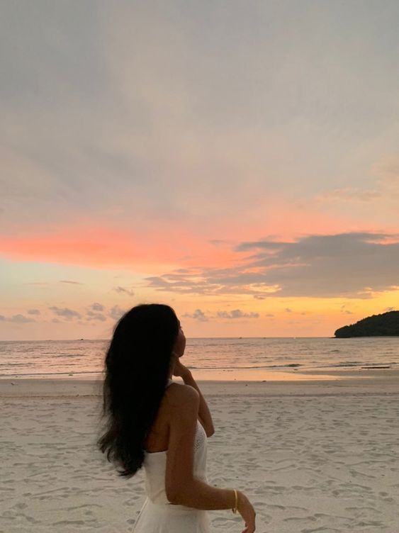 a woman standing on top of a sandy beach next to the ocean at sunset or dawn