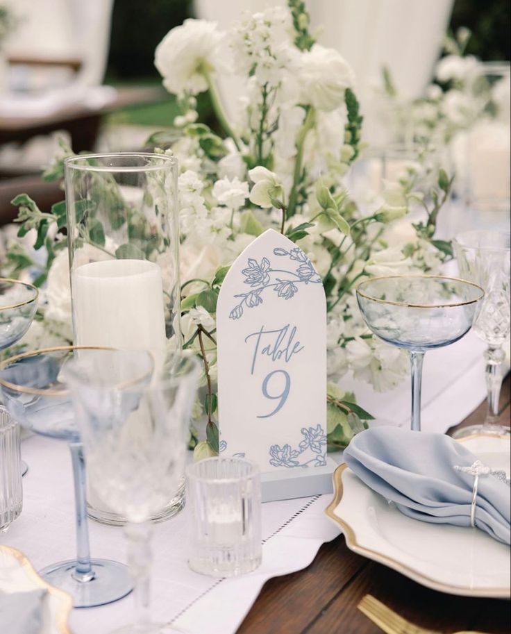 the table is set with white flowers and blue napkins, silverware and candles