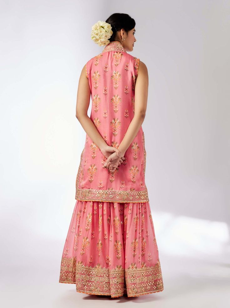 This pretty ensemble of floral jaal, with intricate border embroidery. The sleeveless kurta is embellished down the front and tried with a smart pleated magzi to finish the neckline and armhole. The flowing sharara bottom with gota embroidery still has a lot of flounce and flow. Semi-stitched Sleeveless Dress With Chikankari Embroidery, Semi-stitched Sleeveless Kurta With Mirror Work, Pink Sleeveless Dress For Navratri, Sleeveless Dress With Dori Work For Eid, Sleeveless Pink Dress For Navratri, Sleeveless Chikankari Embroidery Salwar Kameez For Festive Occasions, Sleeveless Anarkali Kurta With Gota Work, Sleeveless Mirror Work Sets For Eid, Sleeveless Eid Sets With Mirror Work