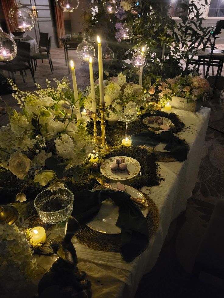 a long table with candles and plates on it in front of a tree filled with flowers