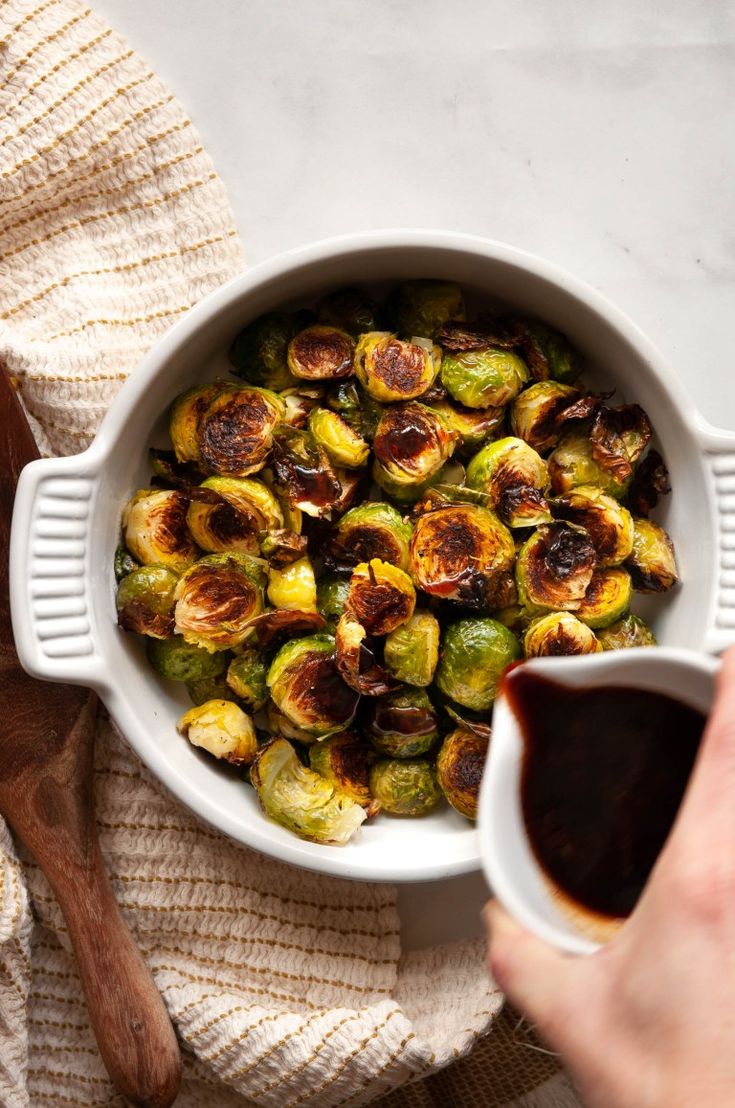 a person dipping sauce into a bowl of roasted brussel sprouts