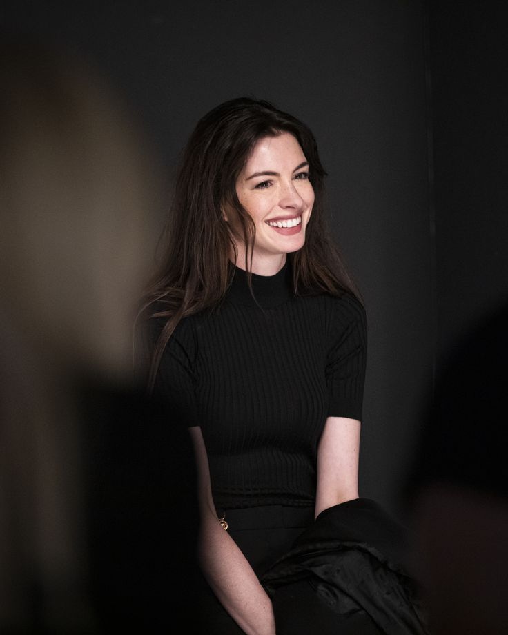 a woman in black dress sitting down and smiling at the camera with her hands on her hips