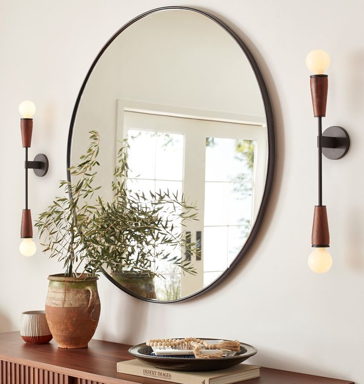 a round mirror hanging on the wall above a table with a plate and potted plant