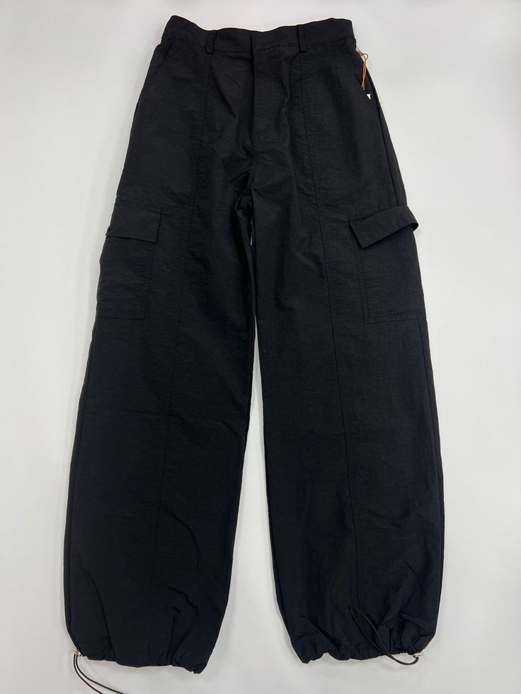 100% Nylon Loose Fit Pants Oversized Pockets on both legs Adjustable toggles at hem Baggy Solid Parachute Pants For Outdoor, Baggy Solid Color Utility Parachute Pants, Solid Color Baggy Utility Parachute Pants, Baggy Solid Utility Parachute Pants, Solid Color Wide Leg Parachute Pants For Outdoor, Solid Color Wide-leg Parachute Pants For Outdoor, Wide Leg Parachute Pants For Outdoor, Solid Wide-leg Techwear Parachute Pants, Outdoor Solid Color Wide-leg Parachute Pants