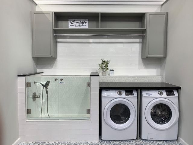 a washer and dryer in a small laundry room with gray cabinets, white tile flooring and built - in shelving