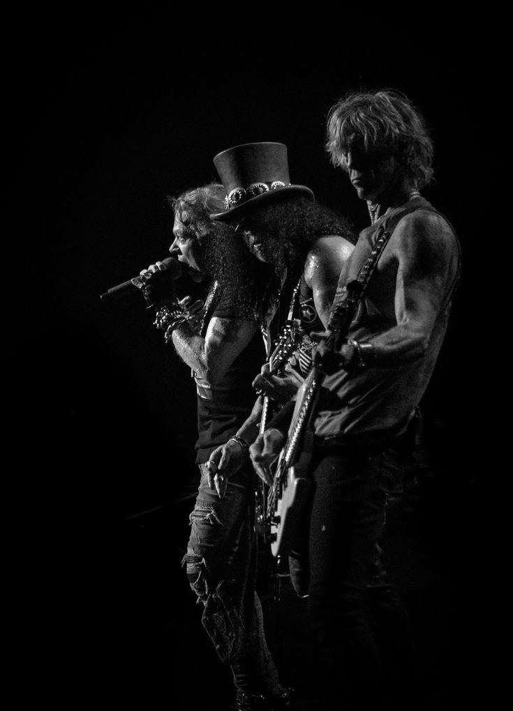 two men with long hair and beards are standing on stage, one wearing a top hat