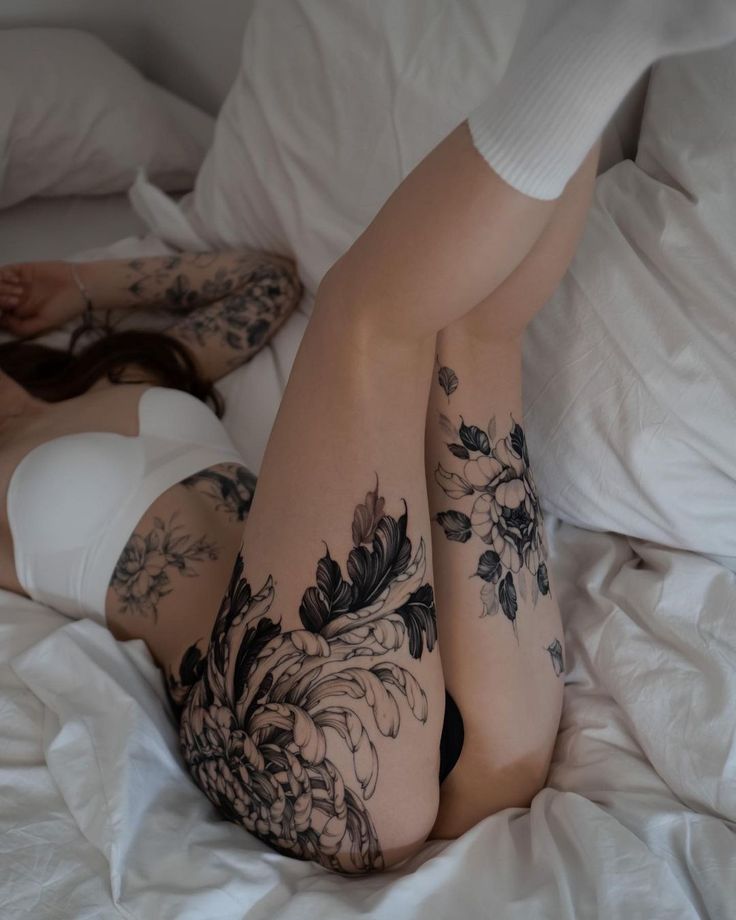 a woman laying on top of a bed covered in white sheets and black ink tattoos