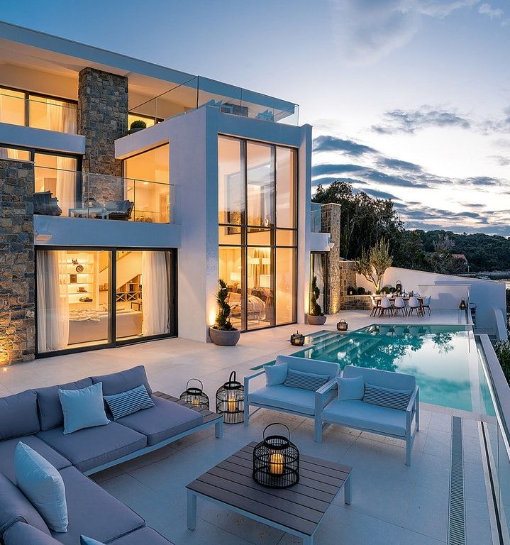 an outdoor living area with couches and tables next to a swimming pool at dusk