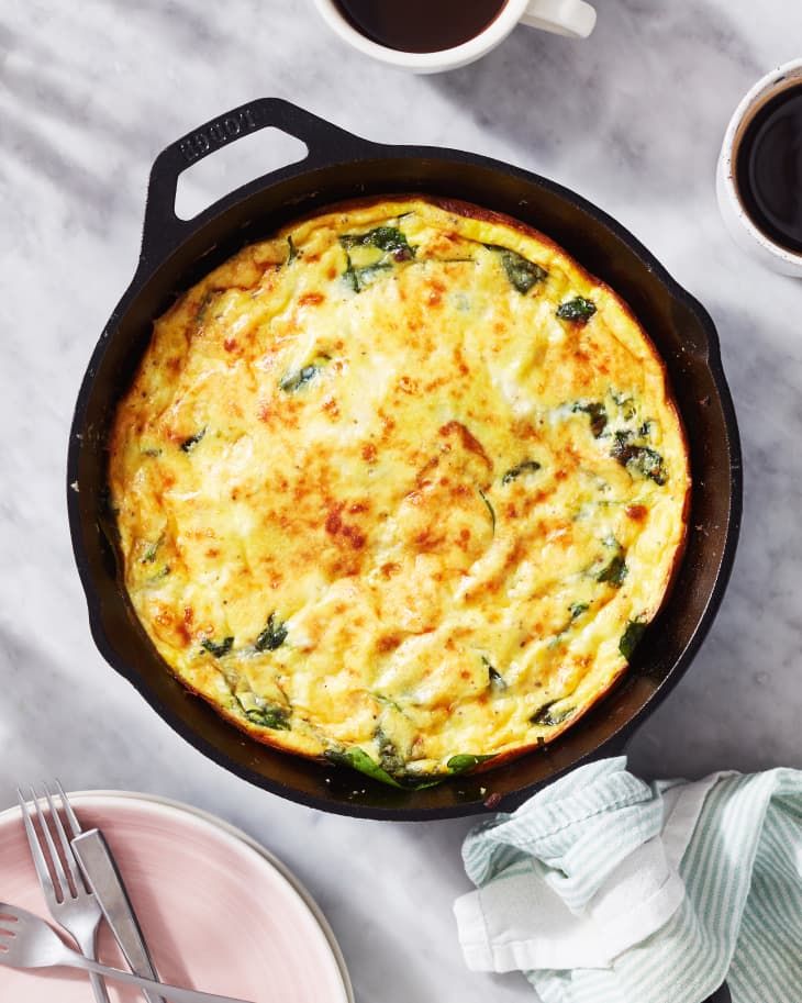 an omelet in a cast iron skillet next to two cups of coffee