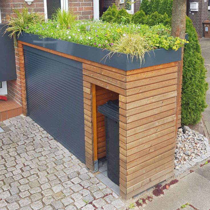 a wooden building with plants growing on the roof and side walls, in front of a brick sidewalk