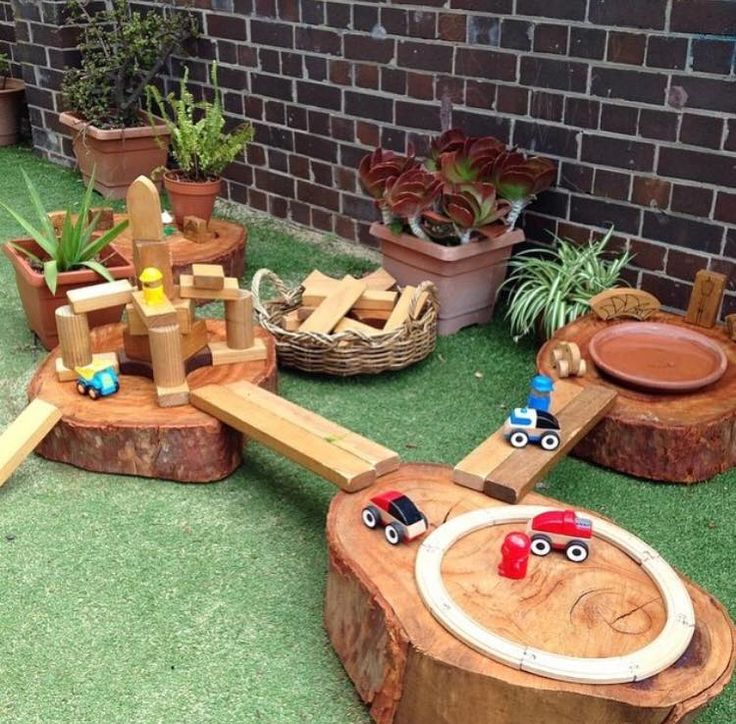 a wooden toy train set sitting on top of a lush green field next to a brick wall