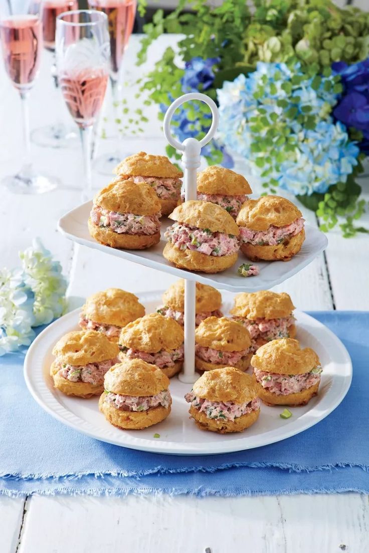 a three tiered tray with sandwiches and wine glasses on the table next to it