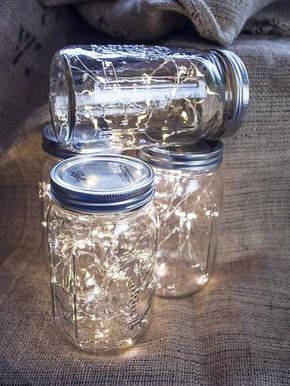 two mason jars with fairy lights in them sitting on a tablecloth covered surface next to a sack