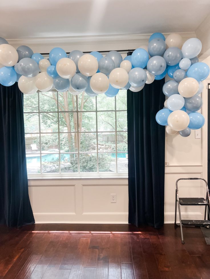 blue and white balloons are hanging from the ceiling in front of a window with black drapes