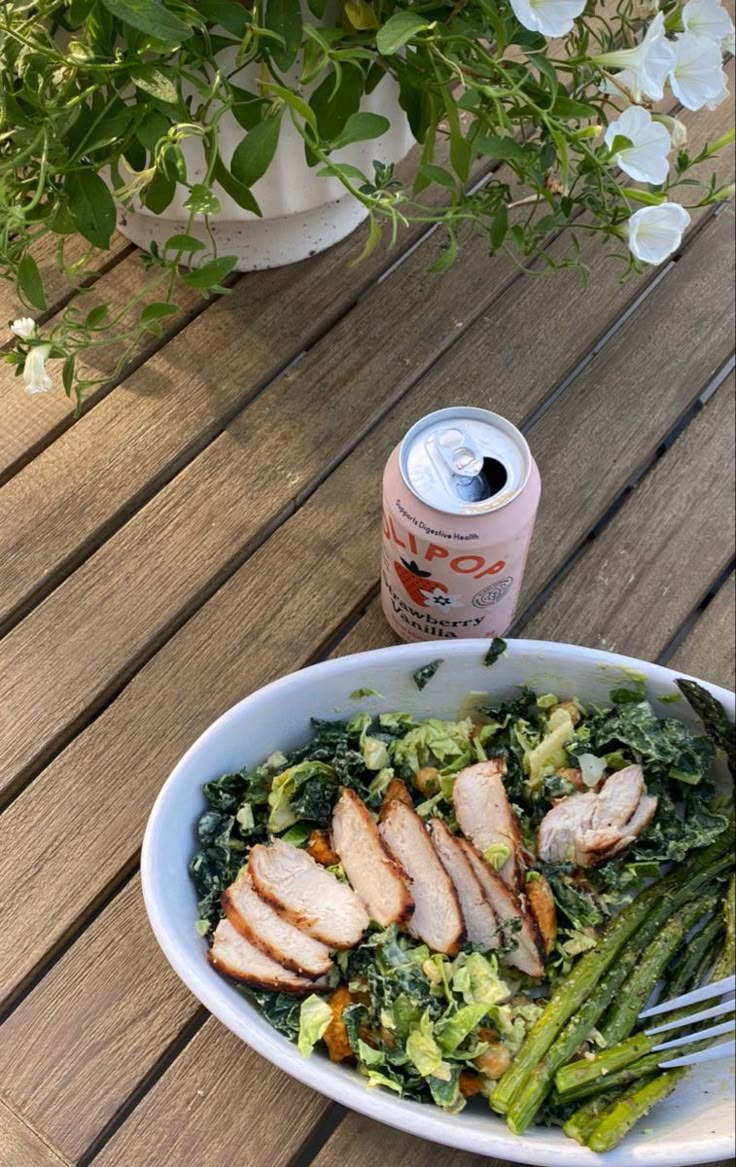 a white bowl filled with meat and veggies next to a can of soda