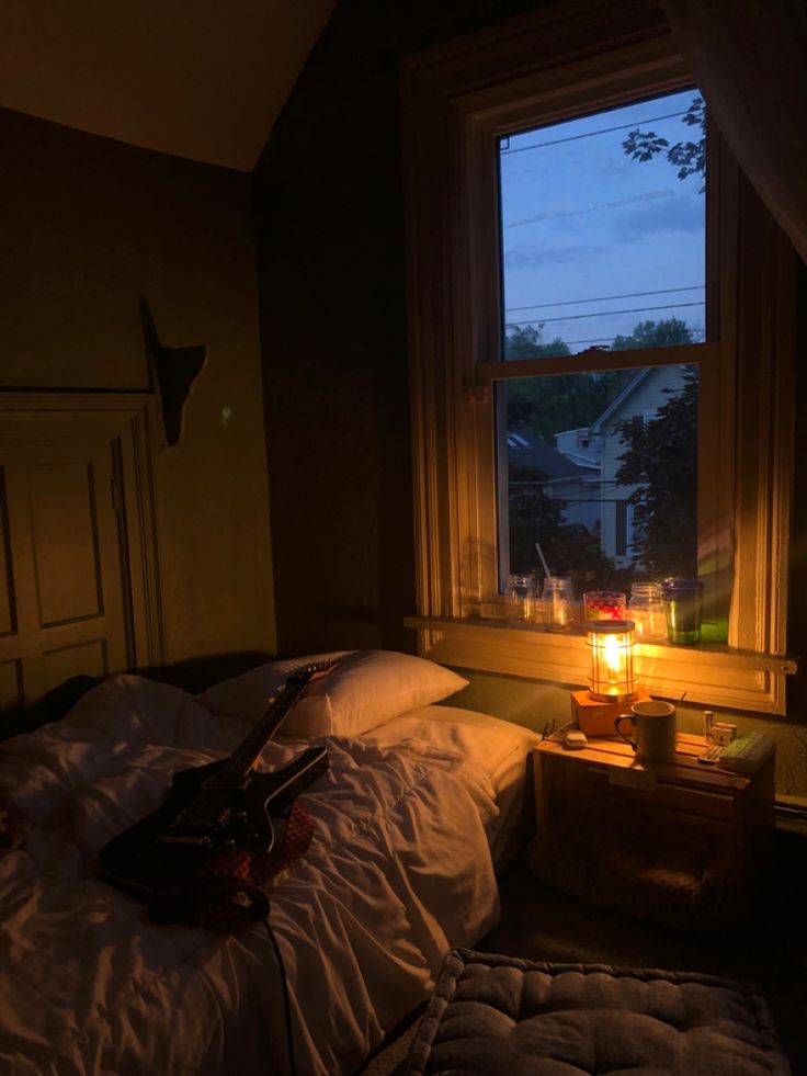 a guitar sitting on top of a bed next to a window with a lit candle