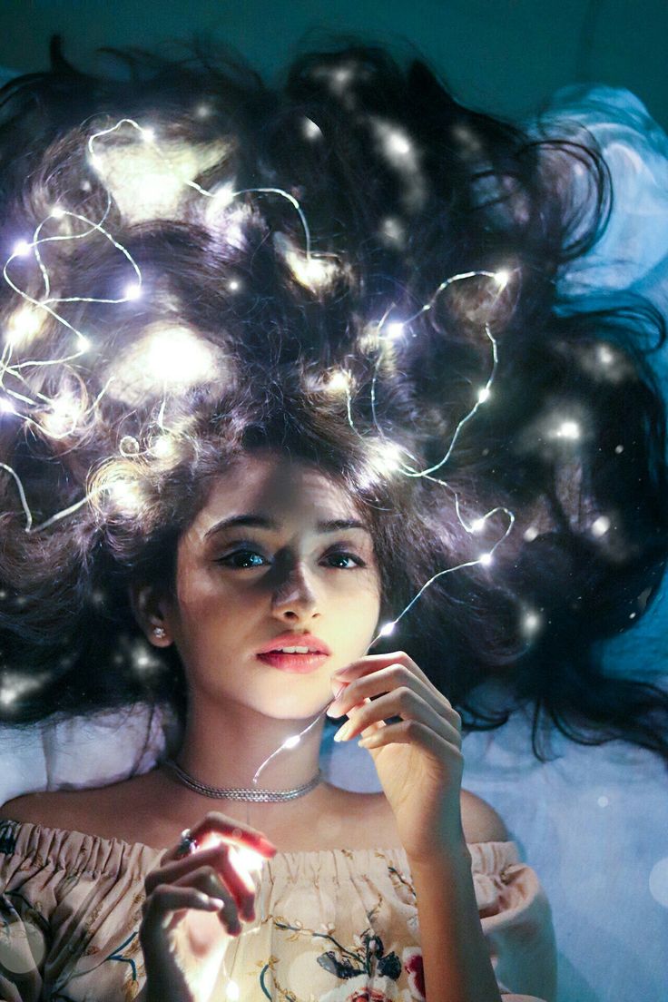 a woman laying on top of a bed with her hair blowing in the wind and lights shining