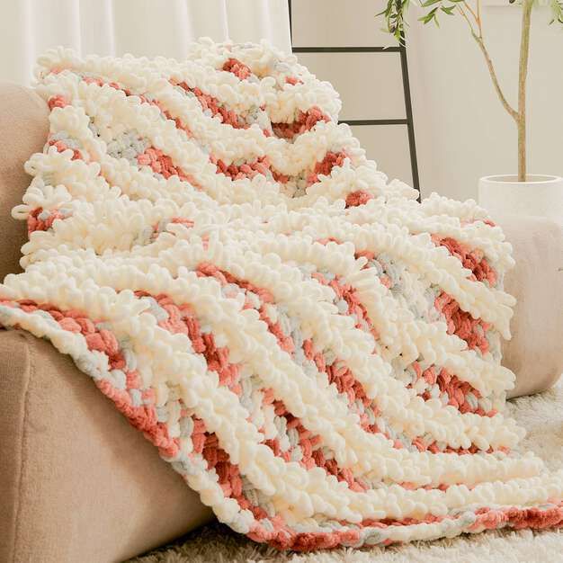 a crocheted blanket sitting on top of a couch next to a potted plant