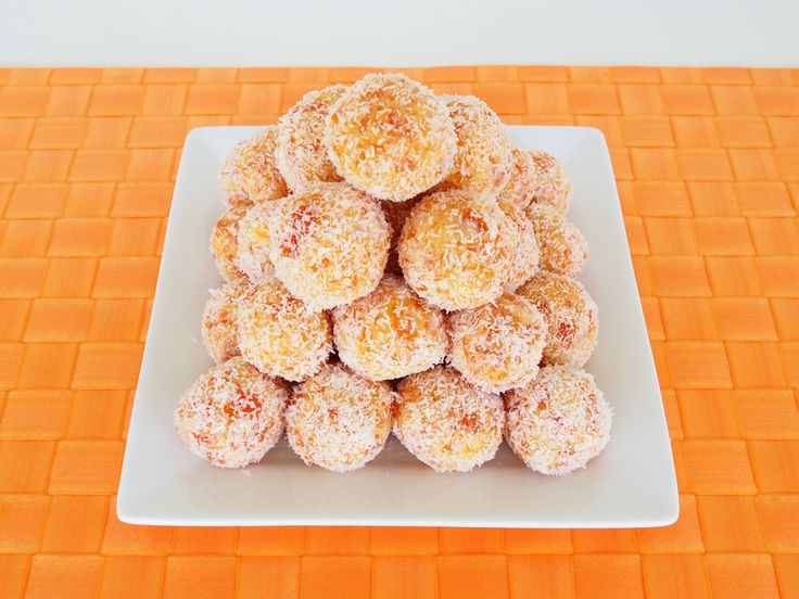 a white plate topped with lots of powdered sugar covered donuts on an orange tablecloth