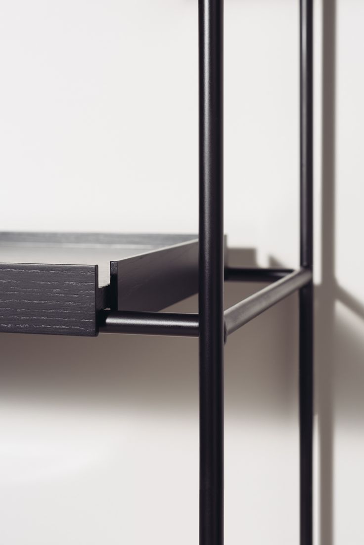 a metal shelf with two black shelves on each side and one white wall in the background