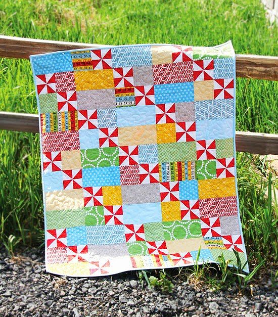 a patchwork quilt hanging on a wooden fence in the grass with green grass behind it