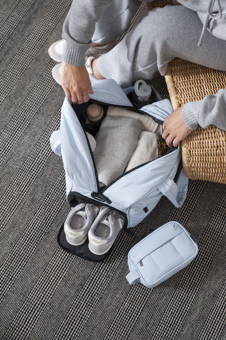 a person sitting on the floor with some clothes in a bag and two pairs of shoes