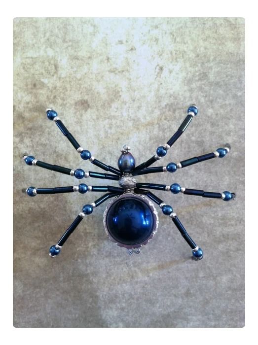 a blue spider brooch sitting on top of a white table next to a black ball