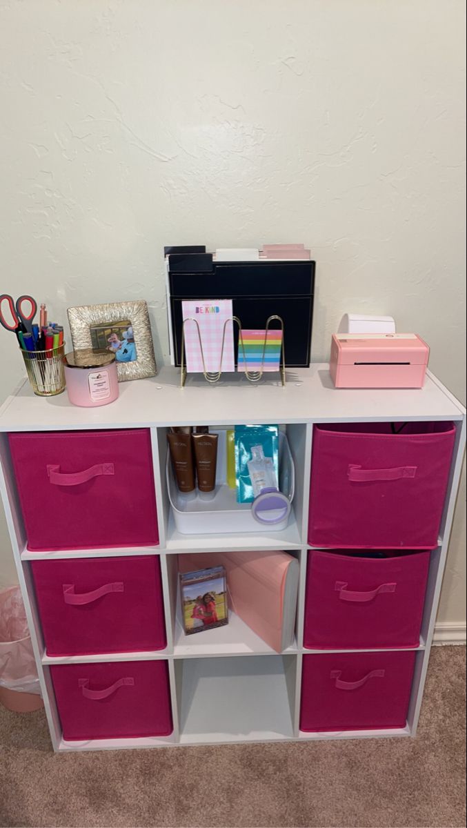 a pink and white shelf with drawers on top of it in front of a wall