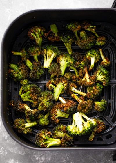 broccoli florets in a black container on a gray counter top with tongs