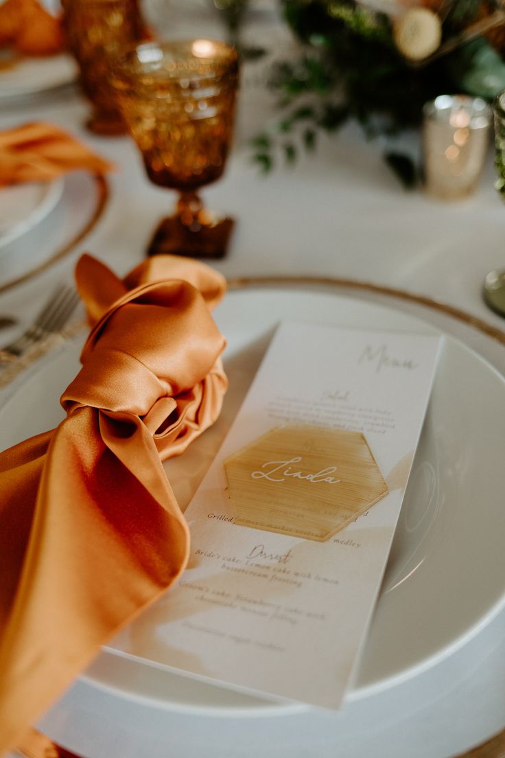 the table is set with white plates and orange napkins, gold rimmed place settings