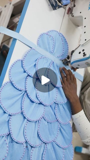 a woman is working on a dress made out of blue fabric and paper with scissors