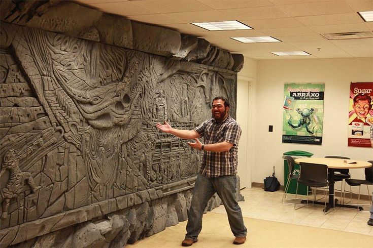 a man standing in front of a stone wall with carvings on it and people sitting at tables