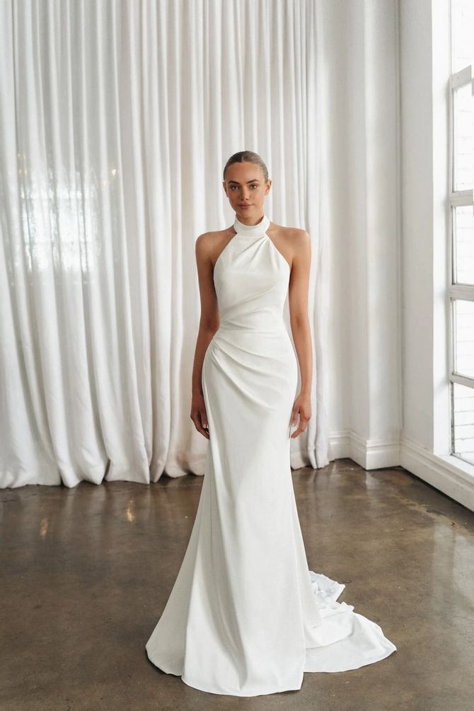 a woman standing in front of a window wearing a white dress