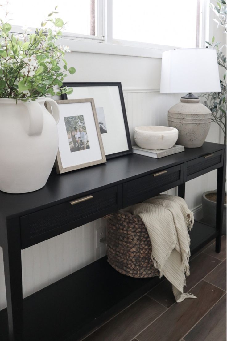 a black table with two white vases and pictures on it next to a window