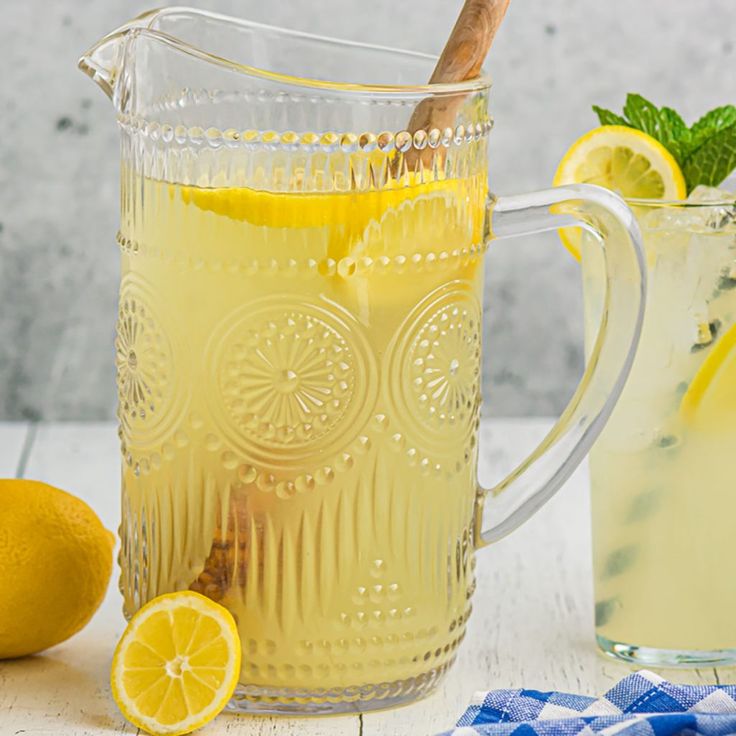 a pitcher filled with lemonade next to a glass cup full of lemonade and a wooden spoon